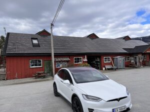 White Tesla Model X parked in front of a building with solar planels in Sandane, Norway