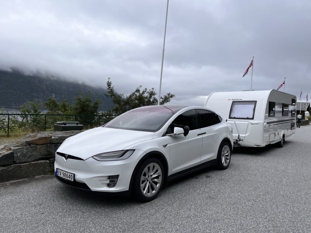 A white Tesla Model X towing a Adra 613PK caravan in beautifyl scenery by a fjord in Norway